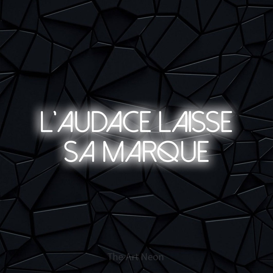 “L'audace laisse sa marque” LED neon sign in cool white, with thin sans-serif lettering across 2 lines, shown against a black polygonal surface.