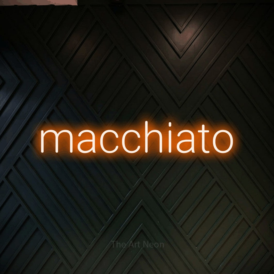 “Macchiato” LED neon sign in orange, with rounded sans-serif lettering, shown against a black chevron-patterned wood wall.