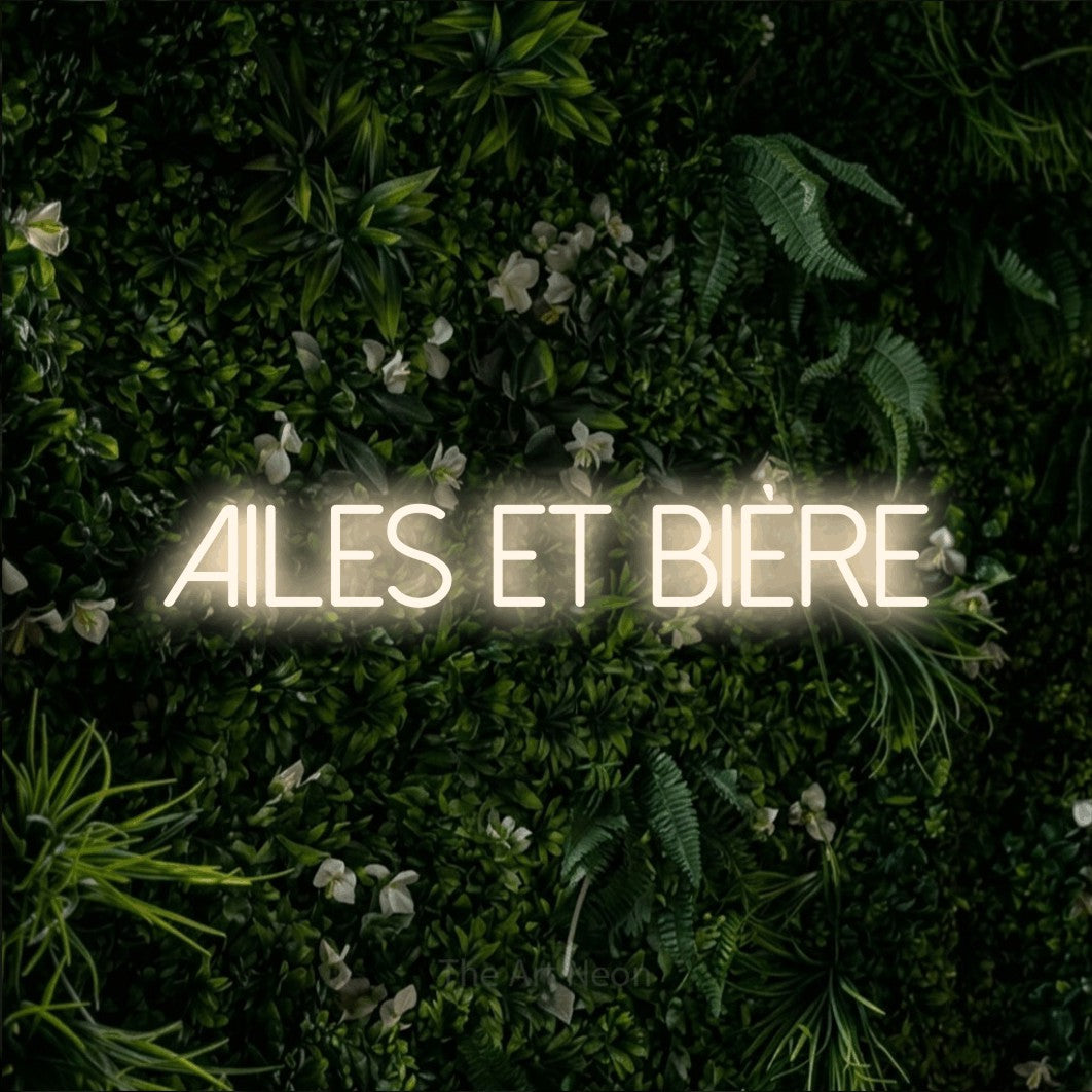 “Ailes et bière” LED neon sign in warm white, with thin sans-serif lettering, shown against a dense green plant wall.