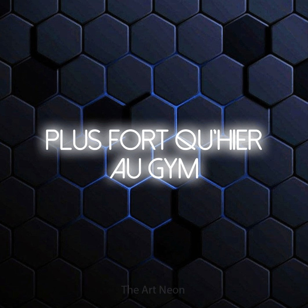 “Plus fort qu'hier au gym” LED neon sign in cool white, with thin sans-serif lettering across 2 lines, shown against a dark blue honeycomb pattern.