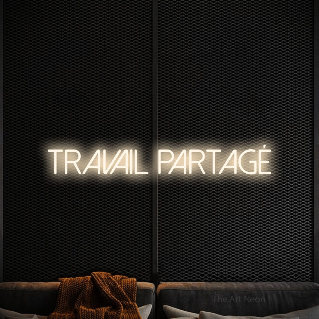 “Travail partagé” LED neon sign in warm white, with thin sans-serif lettering, shown against a modern dark-toned seating area.