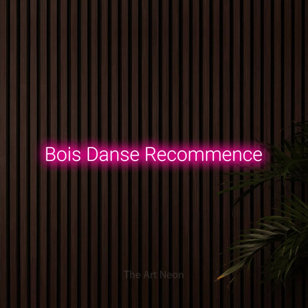 Composition en néon LED « Bois danse recommence » en rose vif, en lettres sans empattement arrondies, mise en valeur sur un mur de lattes en bois foncé, pour un bar ou un pub.