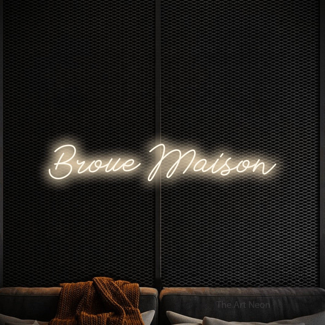 “Broue maison” LED neon sign in warm white, with cursive lettering, shown against a modern dark-toned seating area.