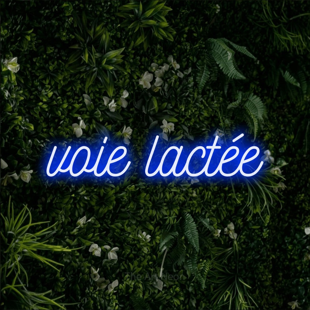 “Voie lactée” LED neon sign in blue, with ornate cursive lettering, shown against a dense green plant wall.
