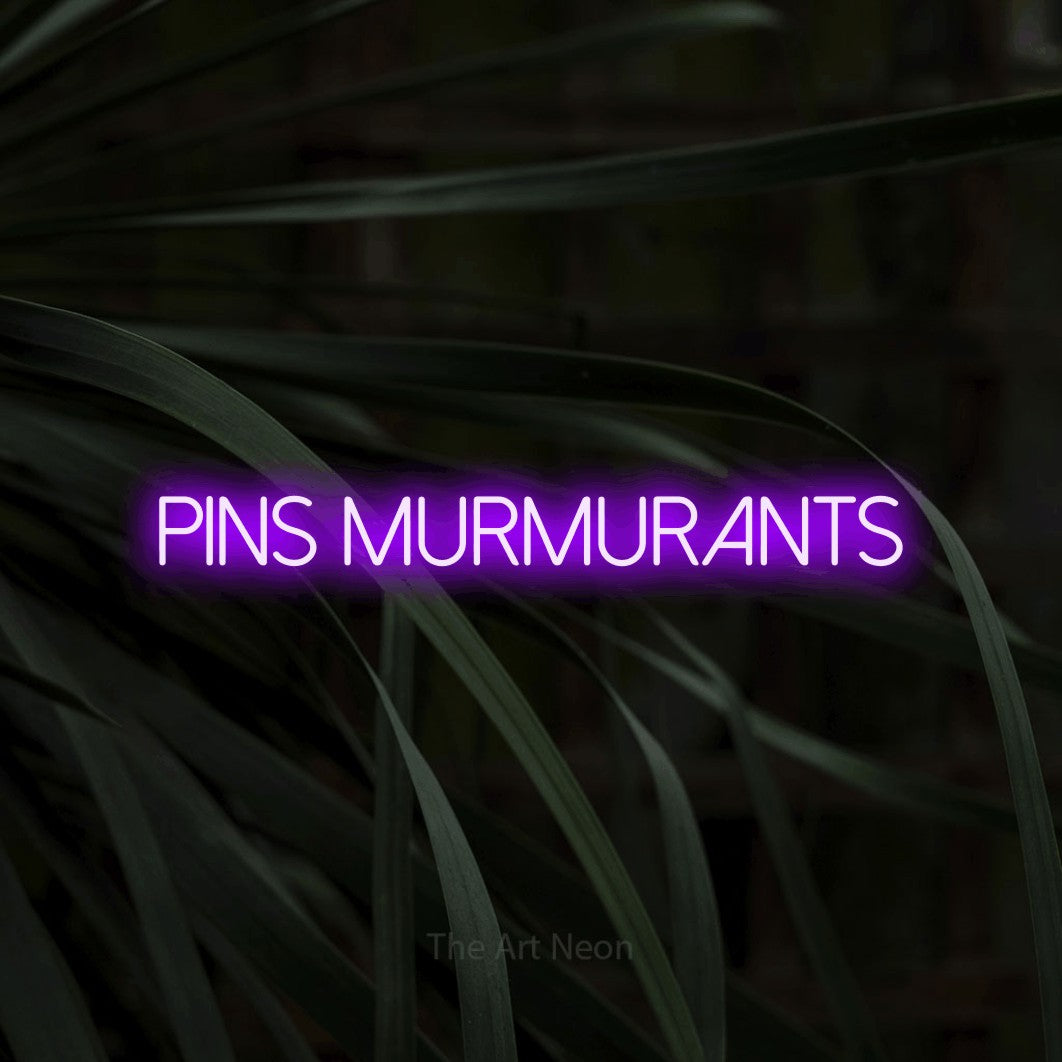 “Pins murmurants” LED neon sign in purple, with thin sans-serif lettering, shown against a close-up of dark foliage.