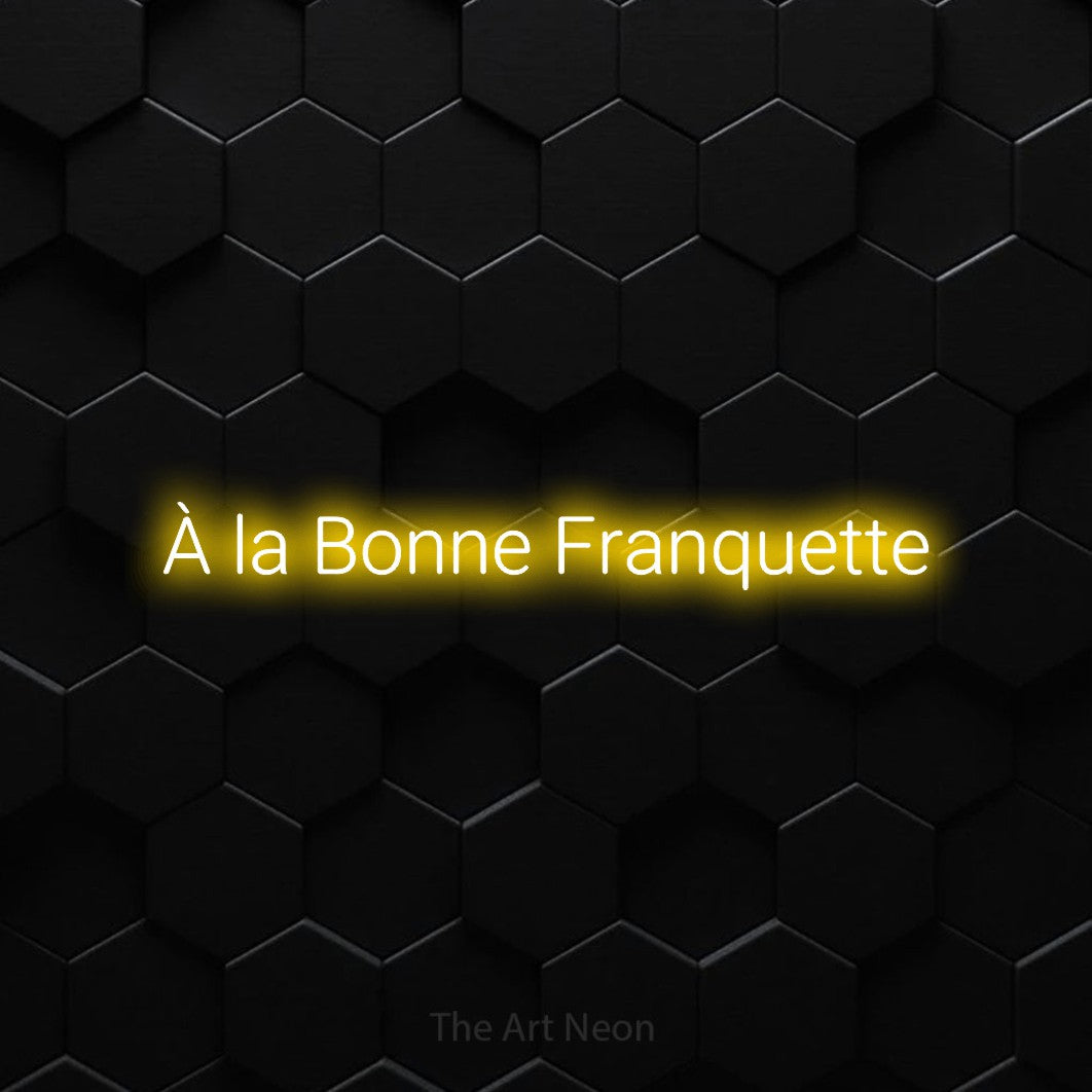 “À la bonne franquette” LED neon sign in yellow, with rounded sans-serif lettering, shown against black hexagonal wall tiles.
