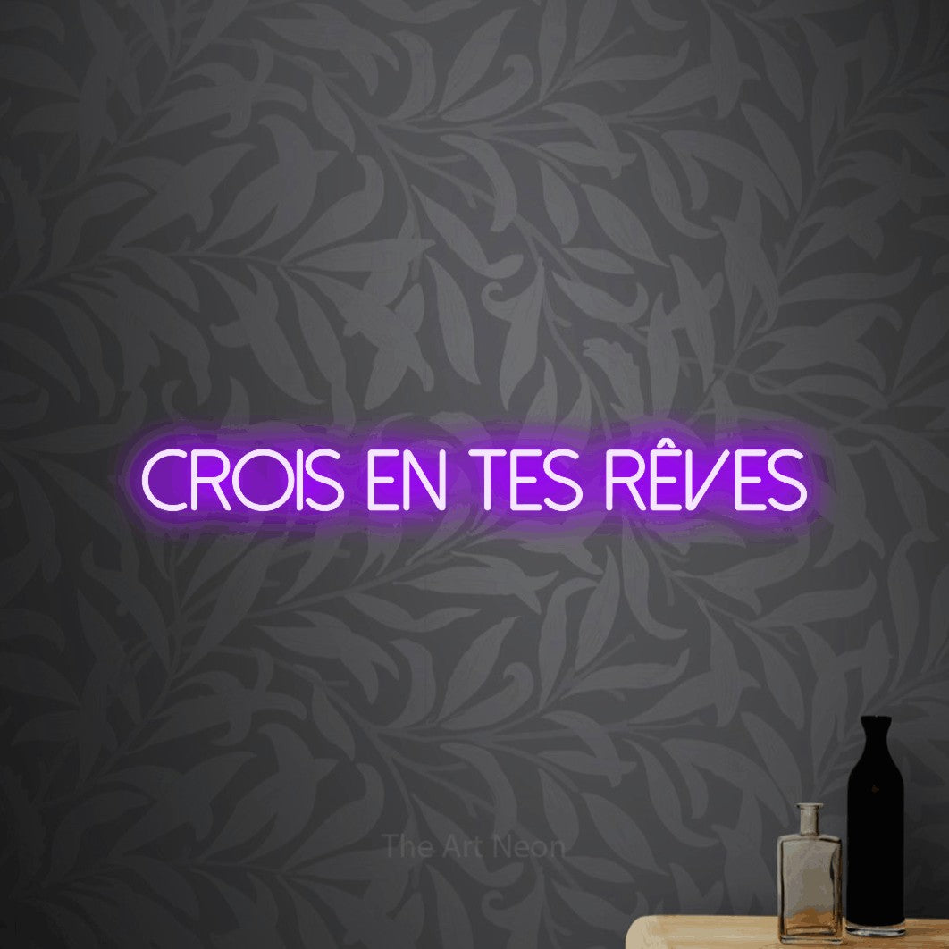 “Crois en tes rêves” LED neon sign in purple, with thin sans-serif lettering, shown against grey botanical wallpaper.