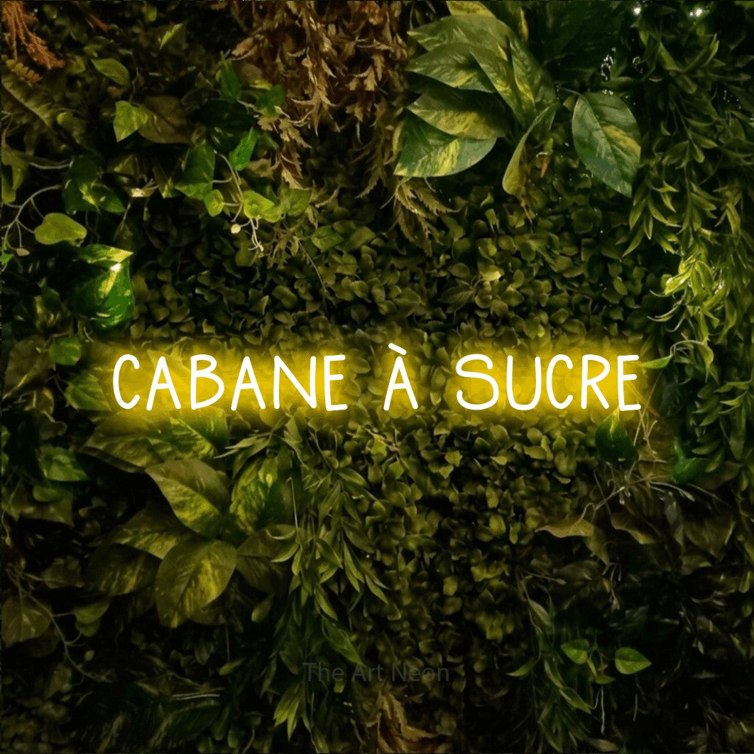 “Cabane à sucre” LED neon sign in yellow, with narrow hand-drawn lettering, shown against bright green and yellow foliage.