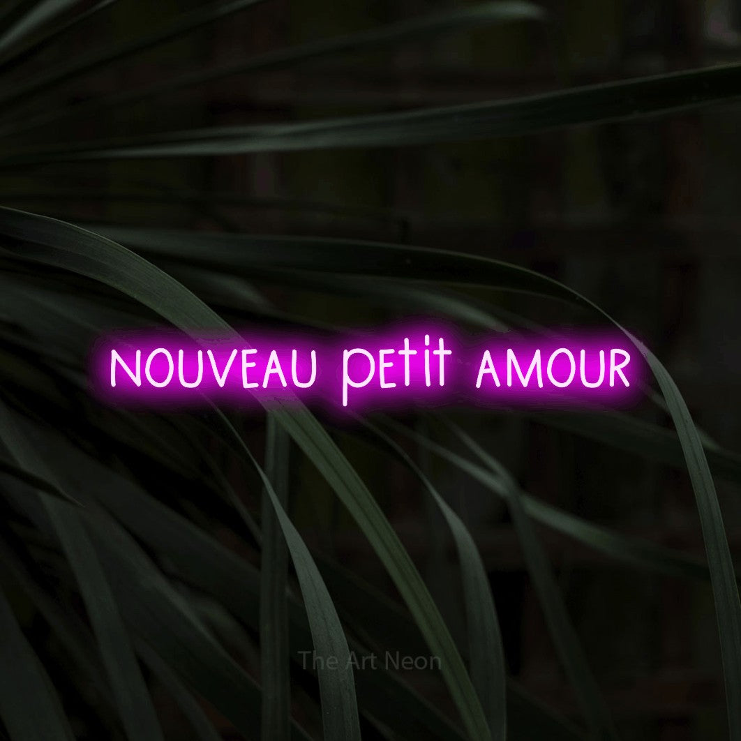 Lettrage en néon LED « Nouveau petit amour » en rose, en lettres étroites dessinées à la main, présenté sur un feuillage sombre en gros plan, pour une fête prénatale.