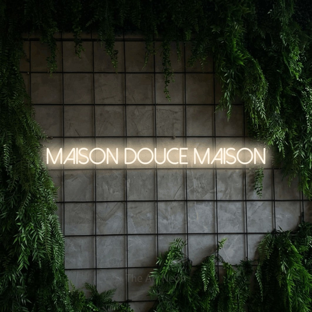 “Maison douce maison” LED neon sign in warm white, with thin sans-serif lettering, shown against an ivy-covered concrete grid.