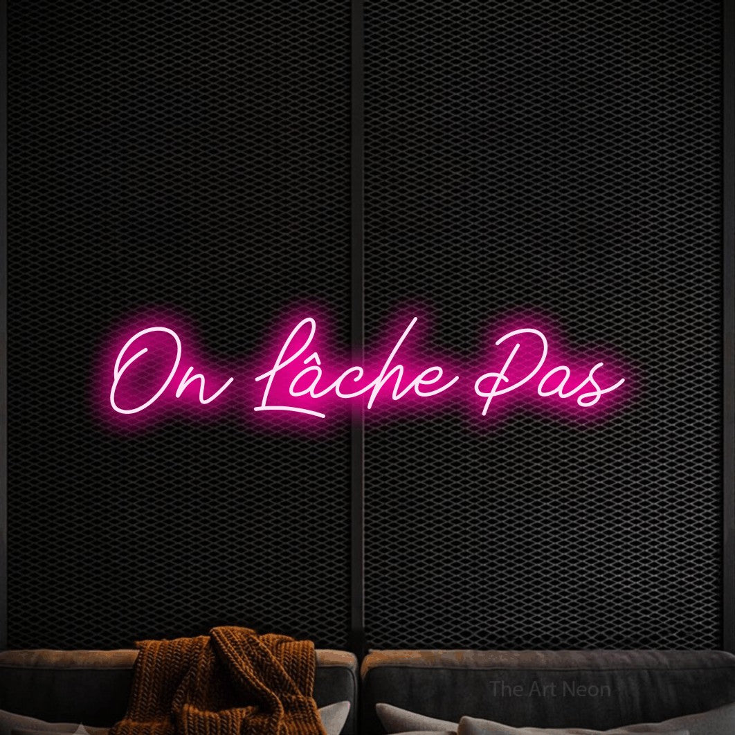 “On lâche pas” LED neon sign in hot pink, with cursive lettering, shown against a modern dark-toned seating area.