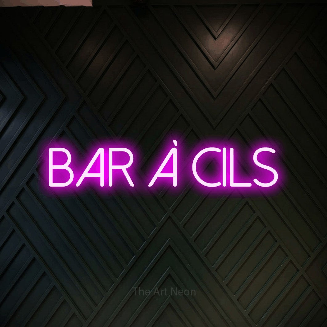 “Bar à cils” LED neon sign in pink, with thin sans-serif lettering, shown against a black chevron-patterned wood wall.