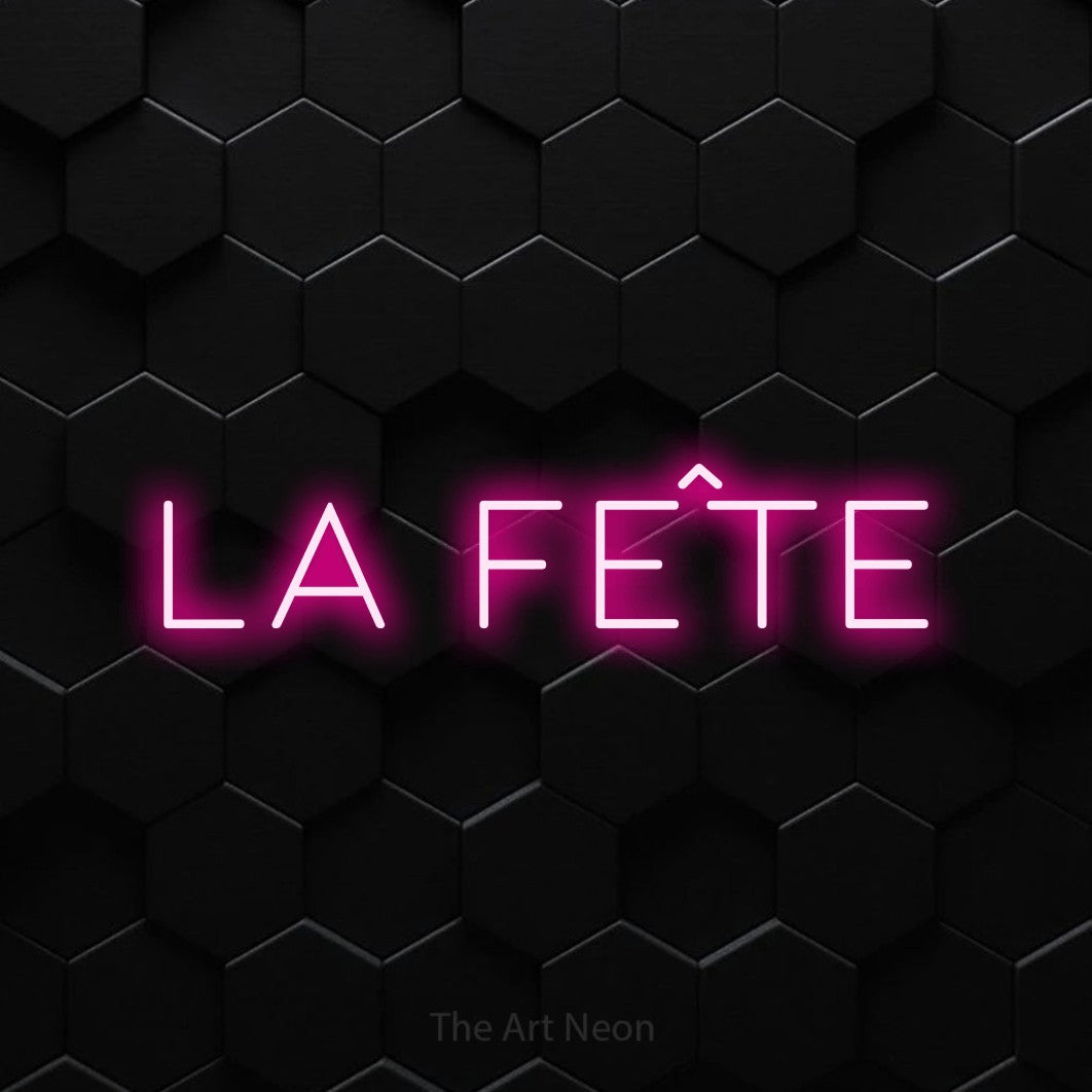 “La fête” LED neon sign in hot pink, with thin, widely spaced lettering, shown against black hexagonal wall tiles.