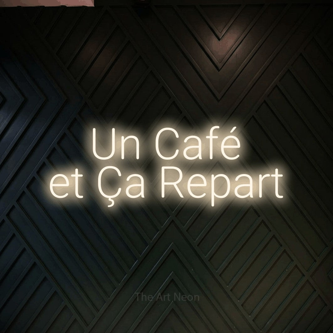 “Un café et ça repart” LED neon sign in warm white, with rounded sans-serif lettering across 2 lines, shown against a black chevron-patterned wood wall.