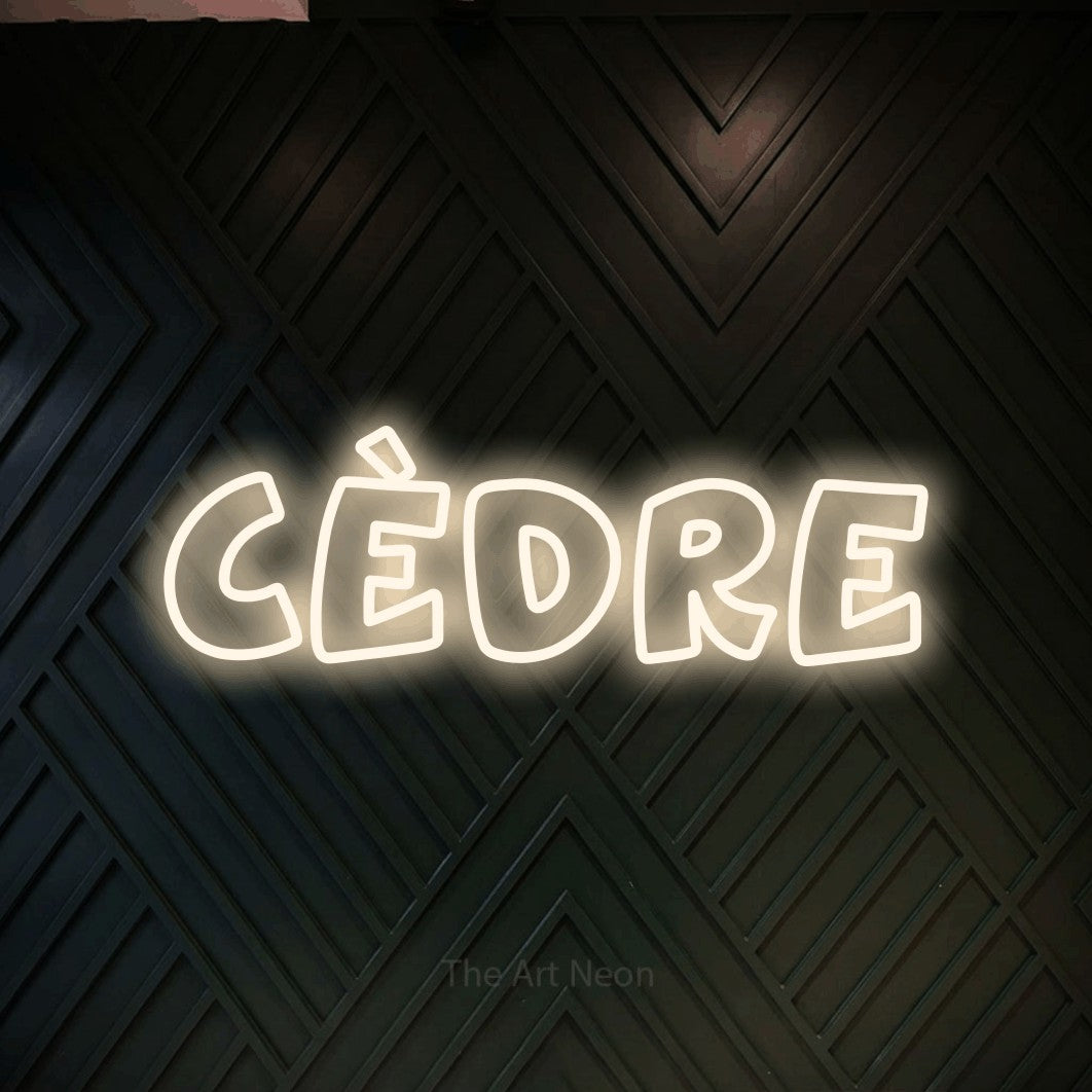 “Cèdre” LED neon sign in warm white, with rounded outline lettering, shown against a black chevron-patterned wood wall.