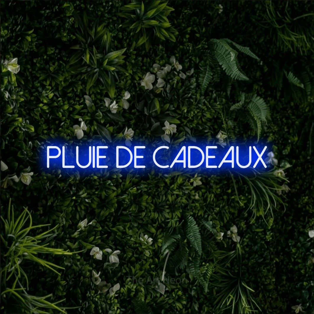 Lettrage en néon LED « Pluie de cadeaux » en bleu, en lettres fines sans empattement, présenté sur un mur végétal vert et dense, pour une fête prénatale.