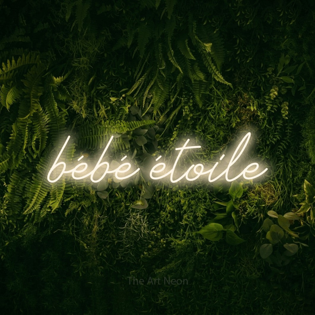 “Bébé étoile” LED neon sign in warm white, with cursive lettering, shown against a dark moss and forest backdrop.