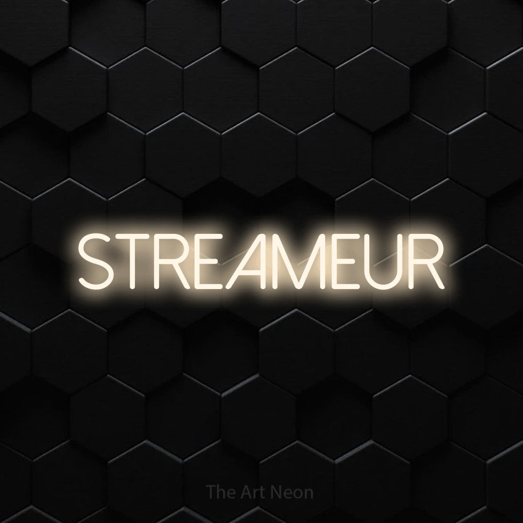“Streameur” LED neon sign in warm white, with thin sans-serif lettering, shown against black hexagonal wall tiles.