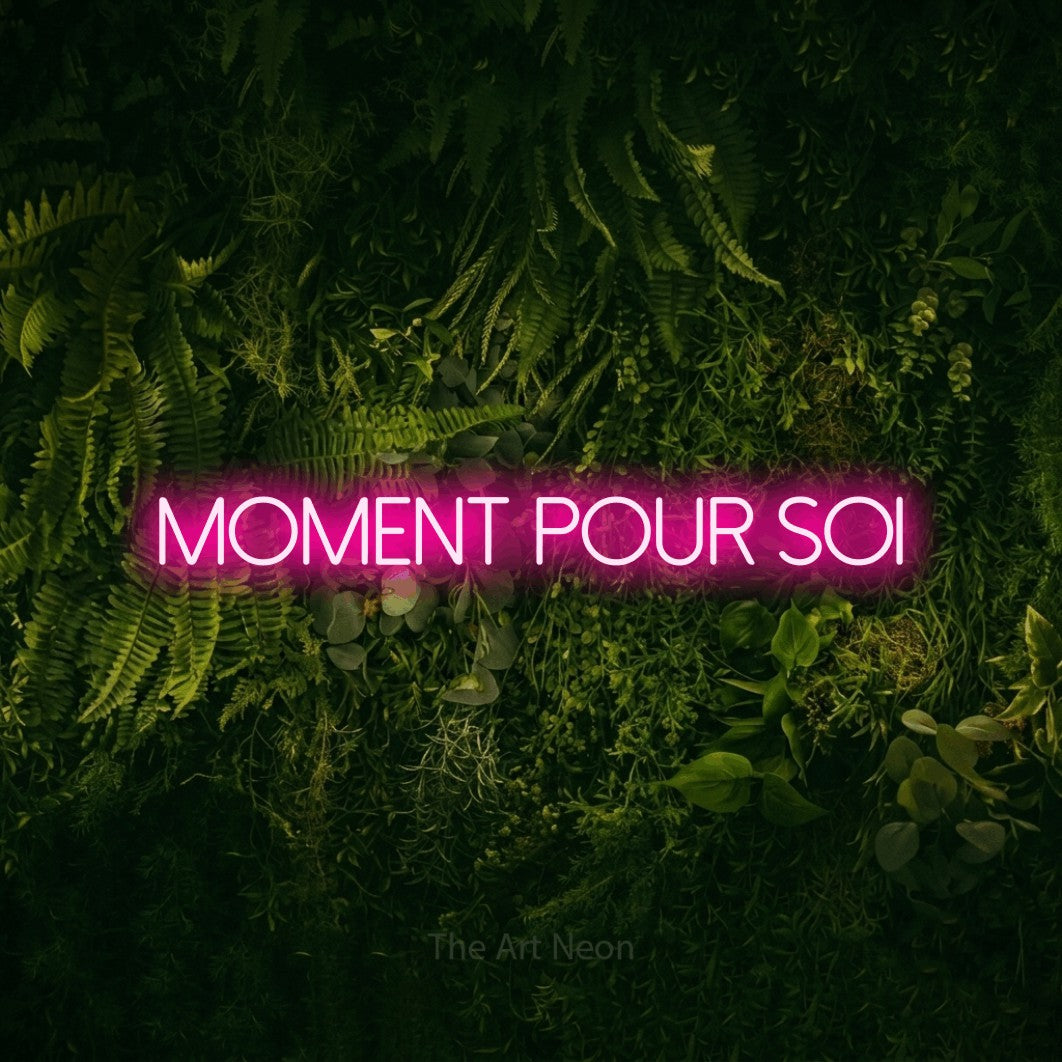 “Moment pour soi” LED neon sign in hot pink, with thin sans-serif lettering, shown against a dark moss and forest backdrop.