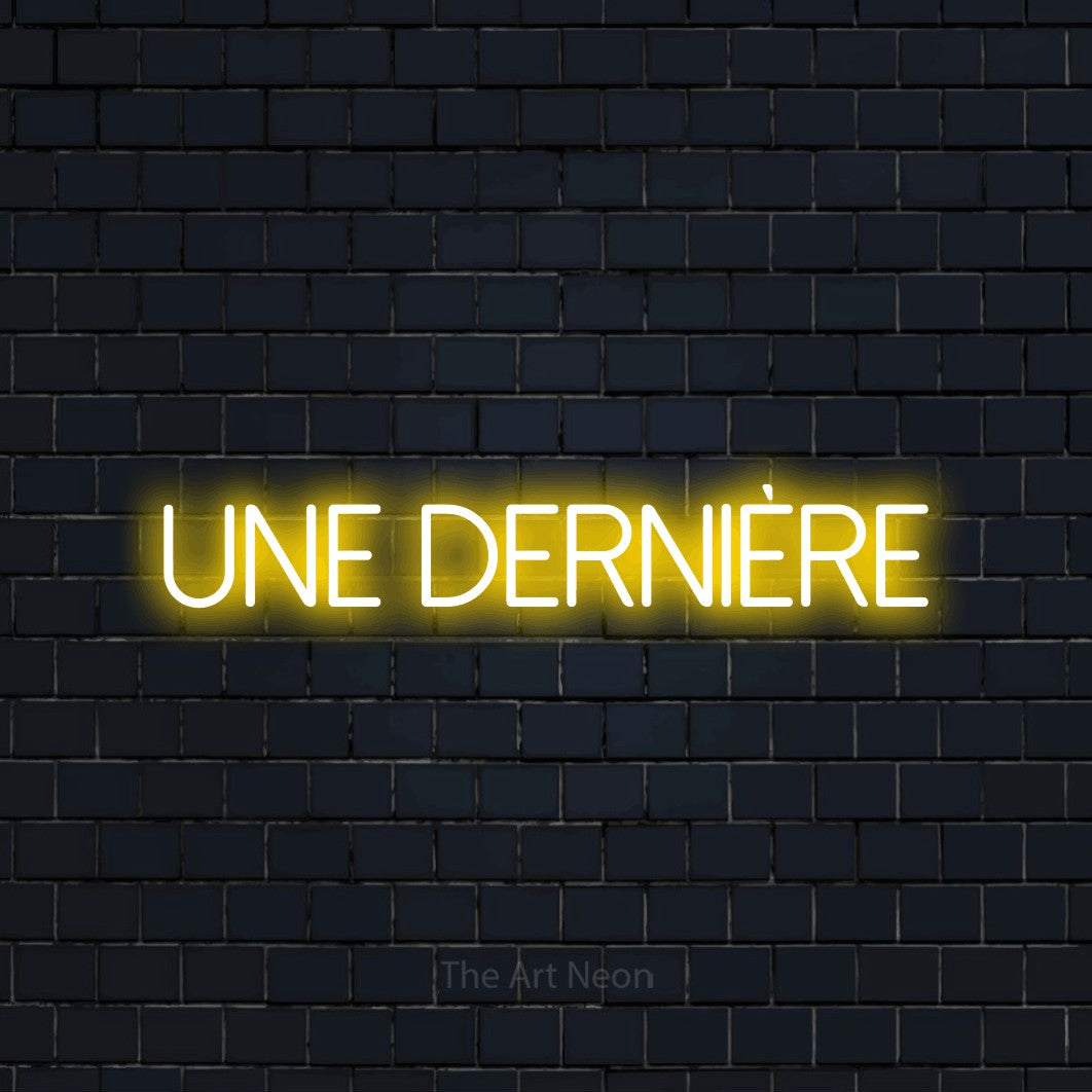 Décoration murale en néon LED « Une dernière » en jaune, en lettres fines sans empattement, installée sur un mur de briques bleu marine foncé, pour un bar à la maison.