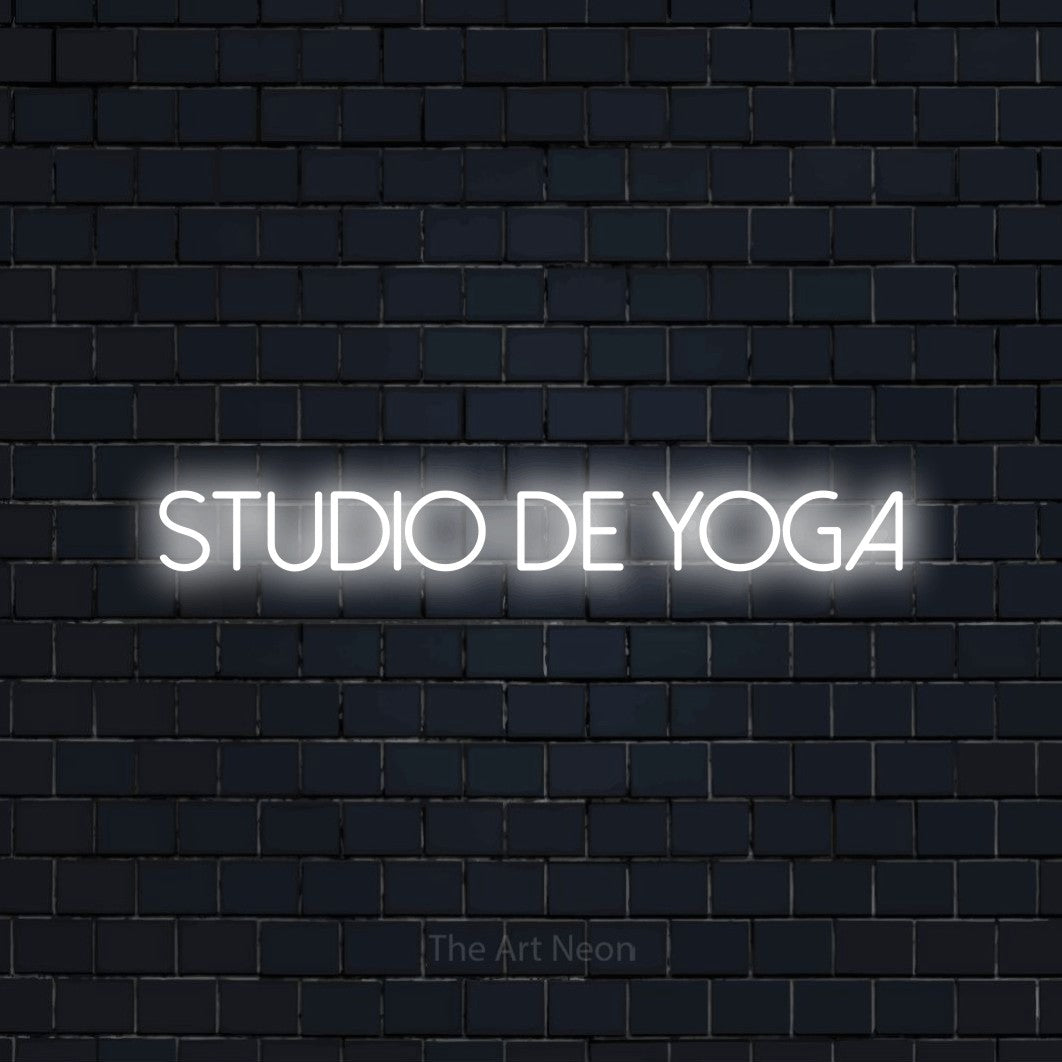 Enseigne néon LED « Studio de yoga » en blanc froid, en lettres fines sans empattement, présentée sur un mur de briques bleu marine foncé, pour un espace d’entraînement.