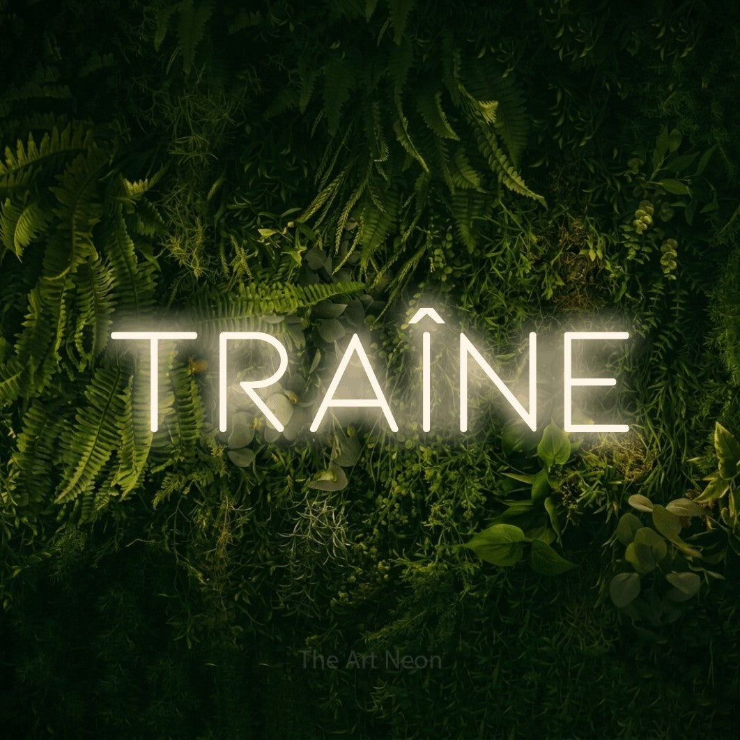 “Traîne” LED neon sign in warm white, with thin, widely spaced lettering, shown against a dark moss and forest backdrop.