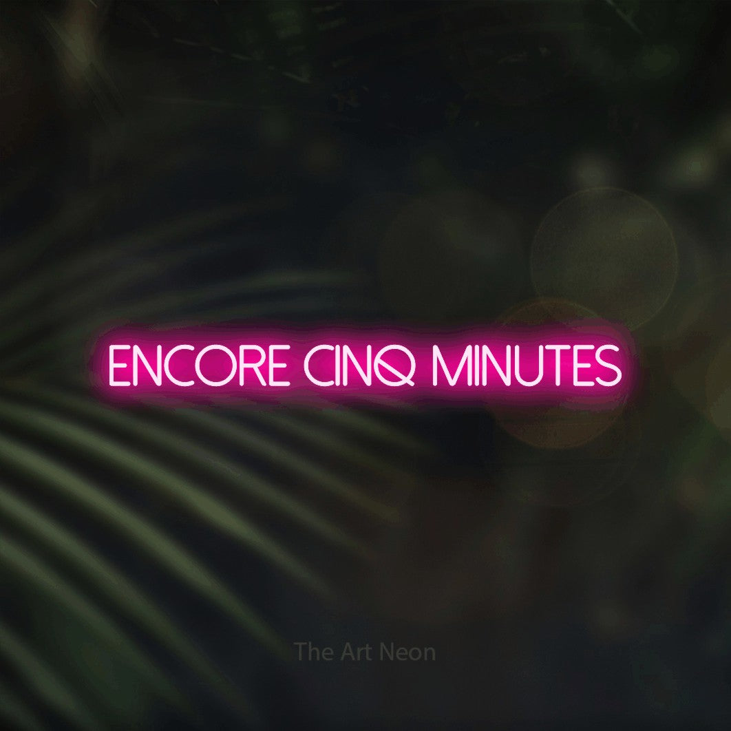 “Encore cinq minutes” LED neon sign in hot pink, with thin sans-serif lettering, shown against a blurred palm and bokeh-light backdrop.