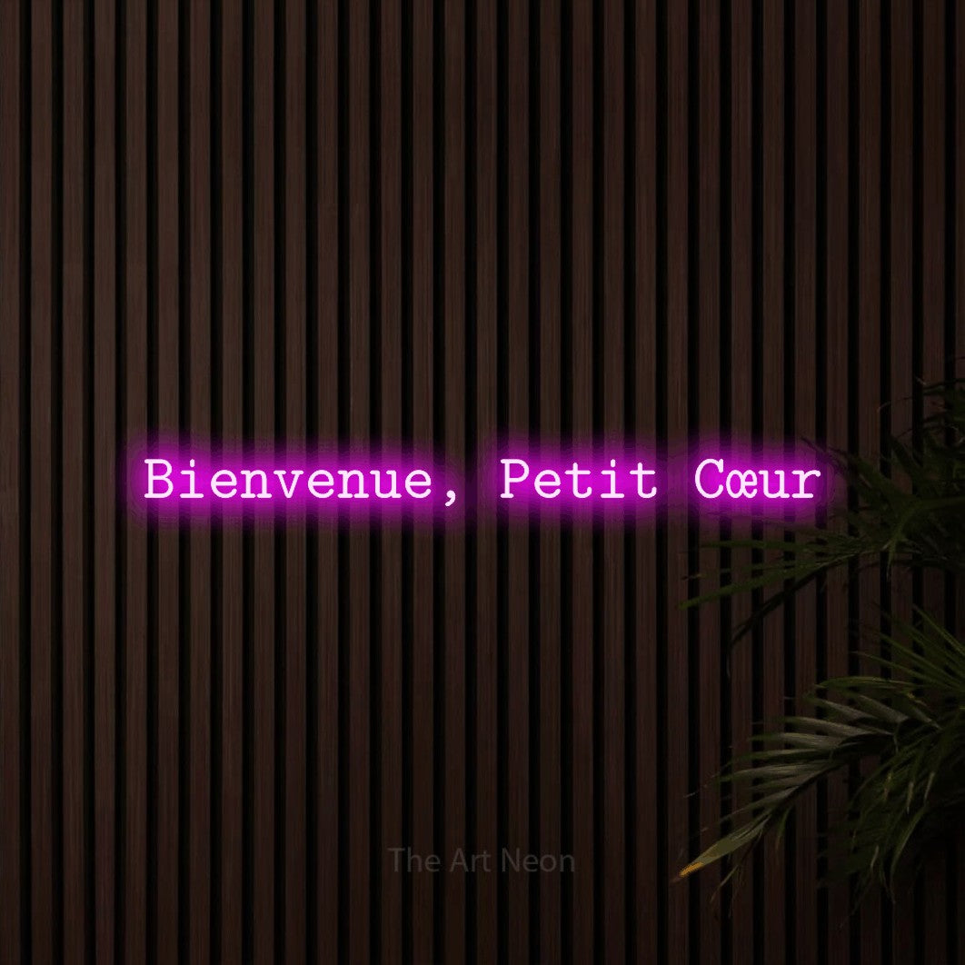 Composition en néon LED « Bienvenue, petit cœur » en rose, en caractères de machine à écrire, mise en valeur sur un mur de lattes en bois foncé, pour une chambre d’enfant.