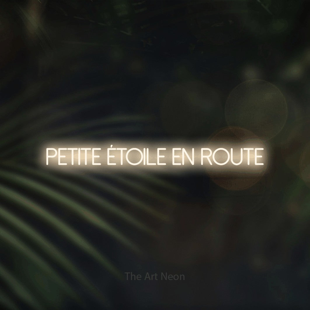 Aperçu d’une enseigne néon LED « Petite étoile en route » en blanc chaud, en lettres fines sans empattement, photographiée sur un fond flou de palmiers et de lumières bokeh, pour une fête prénatale.