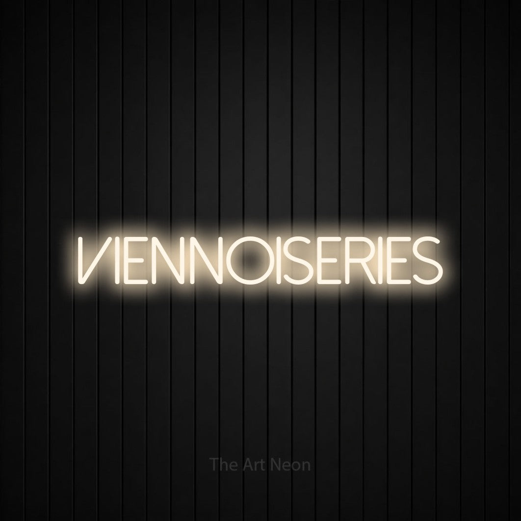 “Viennoiseries” LED neon sign in warm white, with thin sans-serif lettering, shown against black vertical wall slats.
