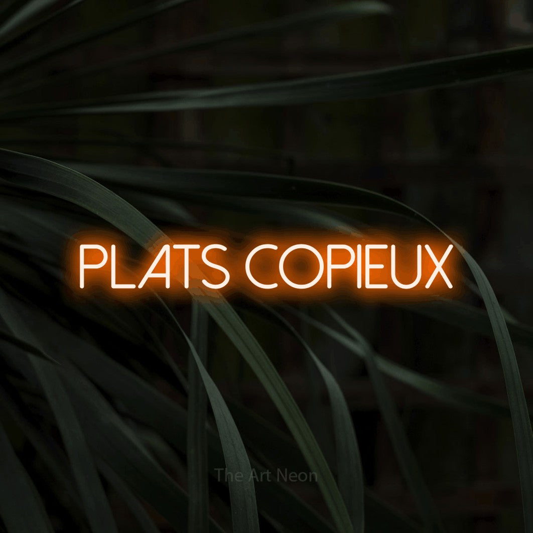 “Plats copieux” LED neon sign in orange, with thin sans-serif lettering, shown against a close-up of dark foliage.