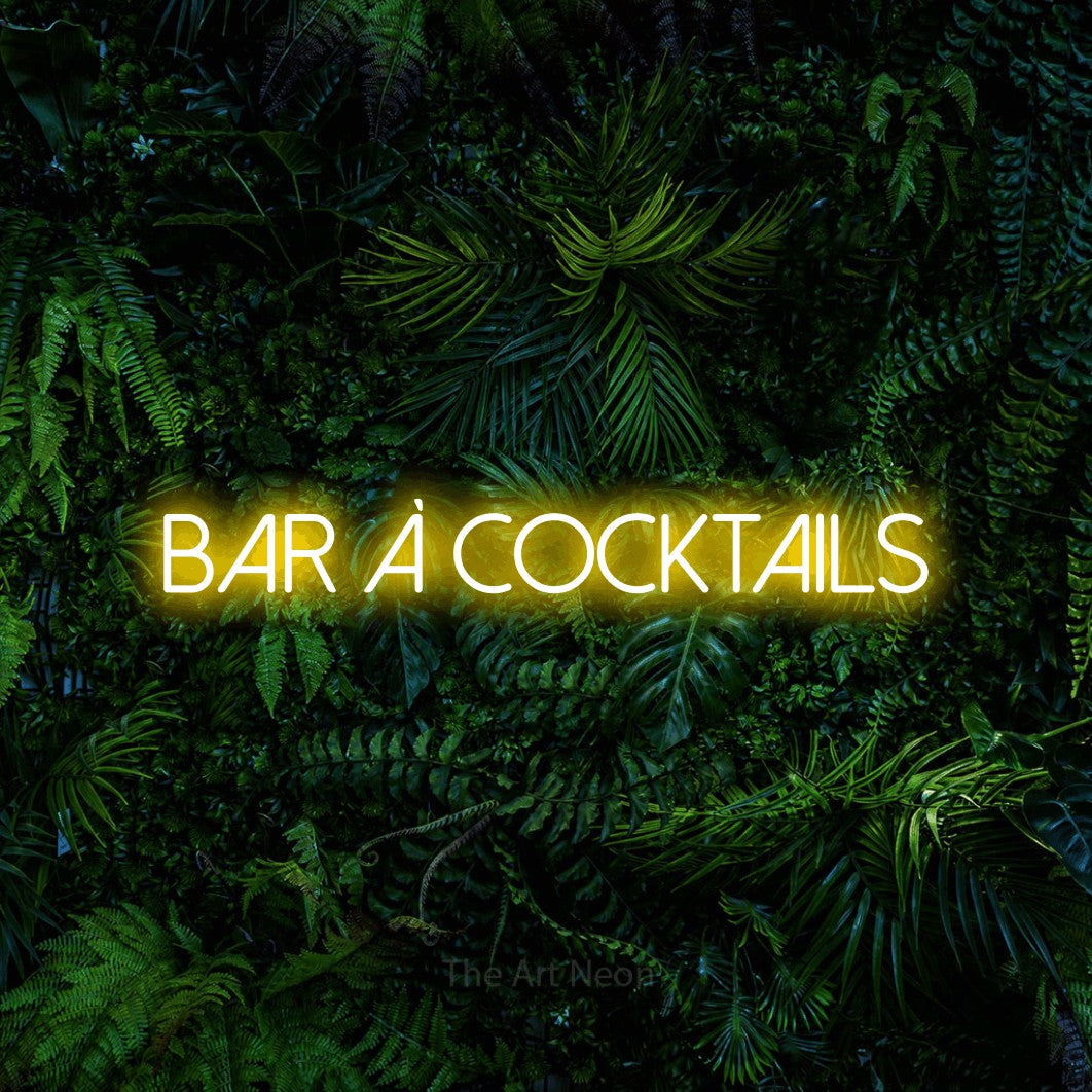 Lettrage en néon LED « Bar à cocktails » en jaune, en lettres fines sans empattement, présenté devant un feuillage tropical dense, pour un bar à la maison.