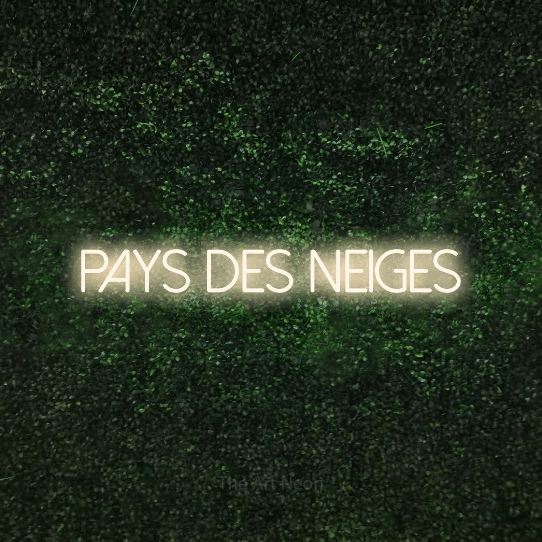 Néon LED « Pays des neiges » en blanc chaud, en lettres fines sans empattement, mis en scène sur une haie verte texturée, pour un décor canadien.