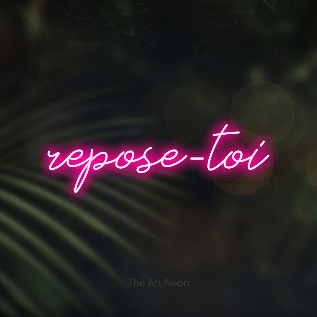 “Repose-toi” LED neon sign in hot pink, with cursive lettering, shown against a blurred palm and bokeh-light backdrop.