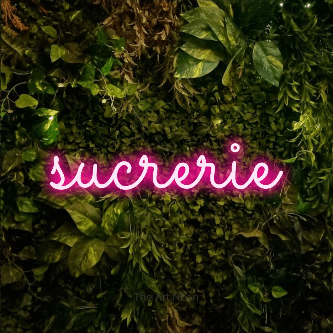“Sucrerie” LED neon sign in hot pink, with looped cursive lettering, shown against bright green and yellow foliage.