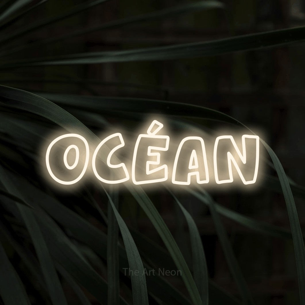“Océan” LED neon sign in warm white, with rounded outline lettering, shown against a close-up of dark foliage.