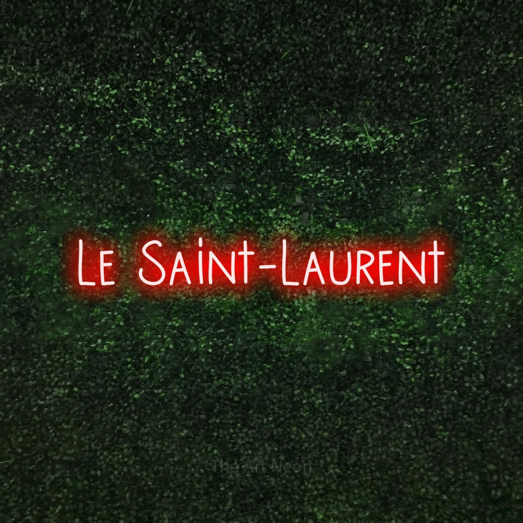 “Le Saint-Laurent” LED neon sign in red, with narrow hand-drawn lettering, shown against a textured green hedge.