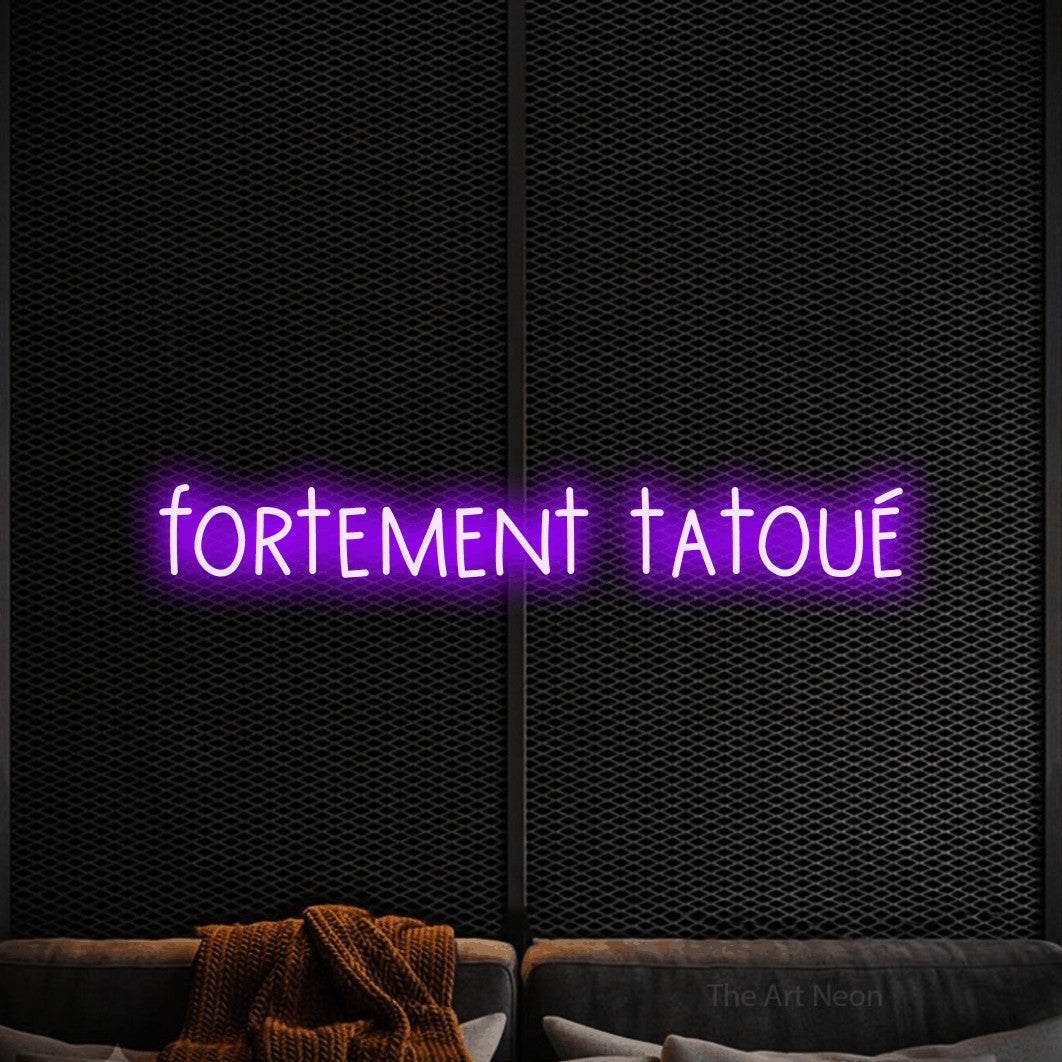 “Fortement tatoué” LED neon sign in purple, with narrow hand-drawn lettering, shown against a modern dark-toned seating area.