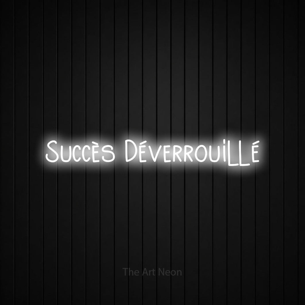 “Succès déverrouillé” LED neon sign in cool white, with narrow hand-drawn lettering, shown against black vertical wall slats.