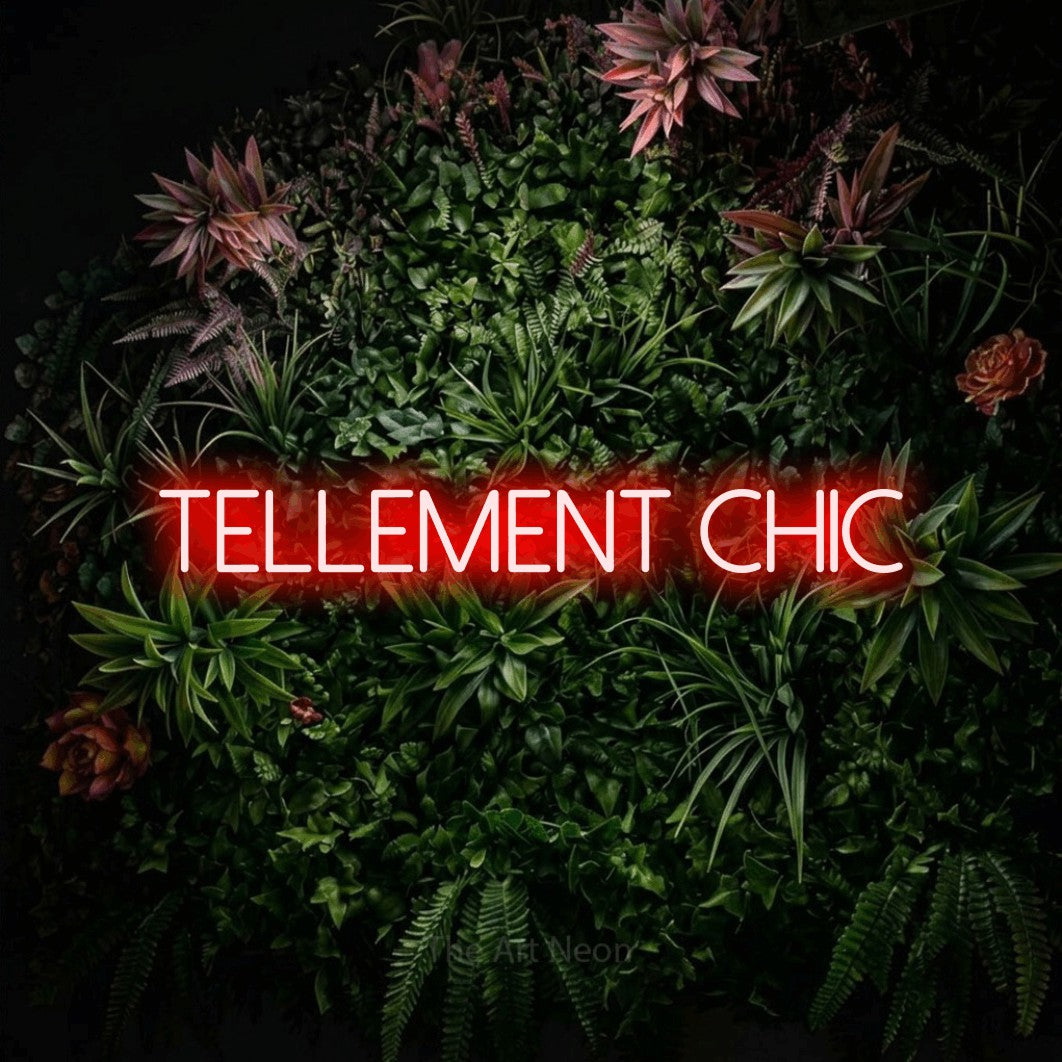 “Tellement chic” LED neon sign in red, with thin sans-serif lettering, shown against a flowering plant wall.