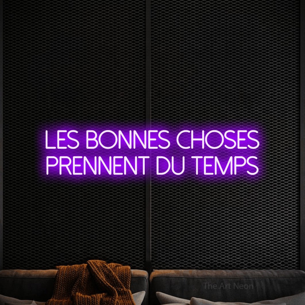 “Les bonnes choses prennent du temps” LED neon sign in purple, with thin sans-serif lettering across 2 lines, shown against a modern dark-toned seating area.