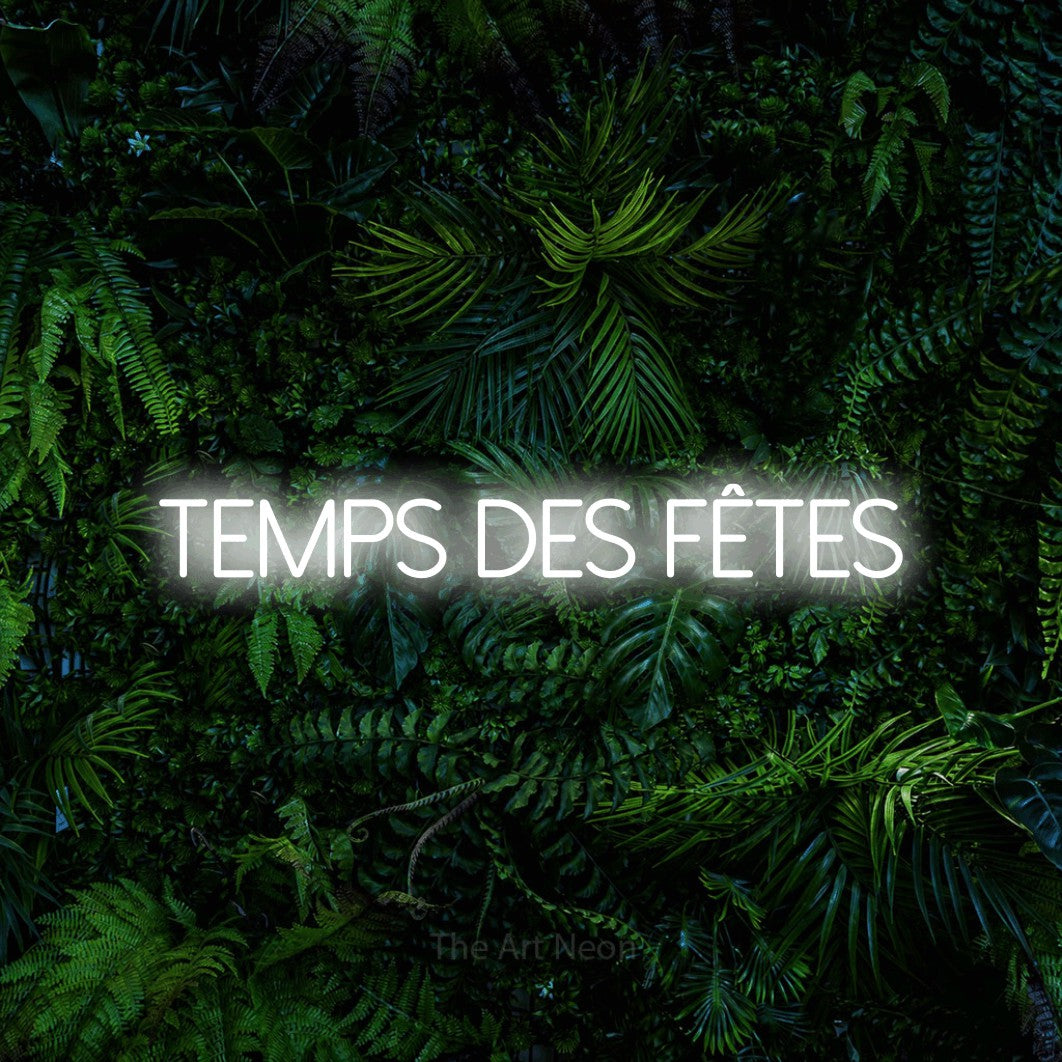 “Temps des fêtes” LED neon sign in cool white, with thin sans-serif lettering, shown against dense tropical foliage.