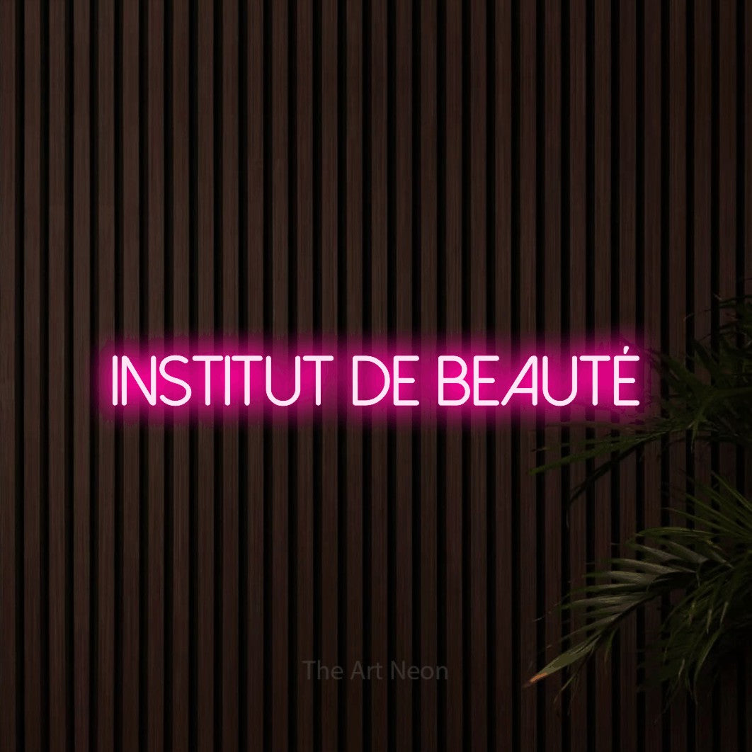Enseigne néon LED « Institut de beauté » en rose vif, en lettres fines sans empattement, présentée sur un mur de lattes en bois foncé, pour un salon de beauté.