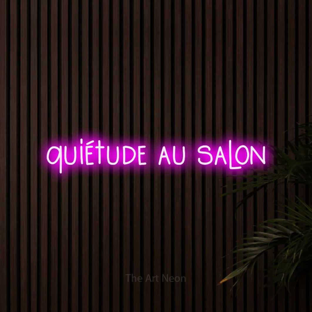 “Quiétude au salon” LED neon sign in pink, with narrow hand-drawn lettering, shown against dark wooden wall slats.