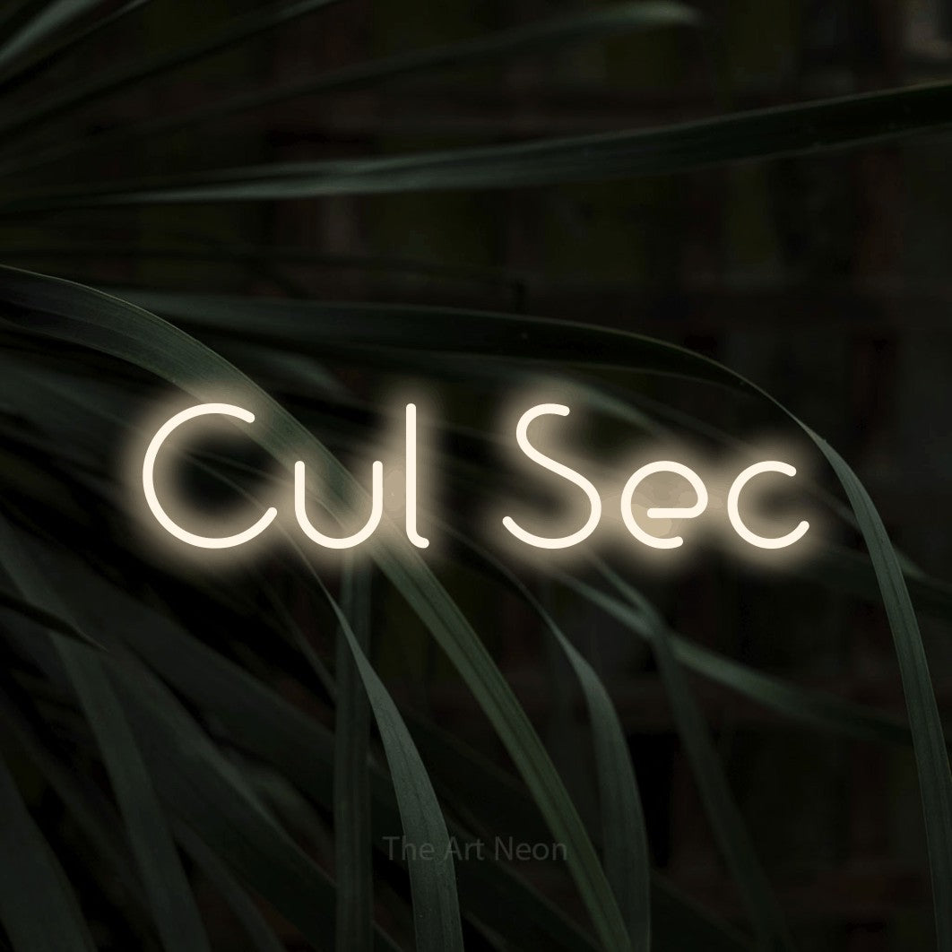Néon LED « Cul sec » en blanc chaud, en lettres géométriques stylisées, mis en scène sur un feuillage sombre en gros plan, pour une cuisine.