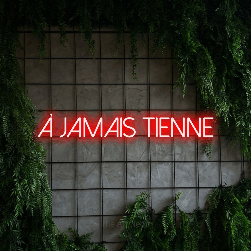 “À jamais tienne” LED neon sign in red, with thin sans-serif lettering, shown against an ivy-covered concrete grid.