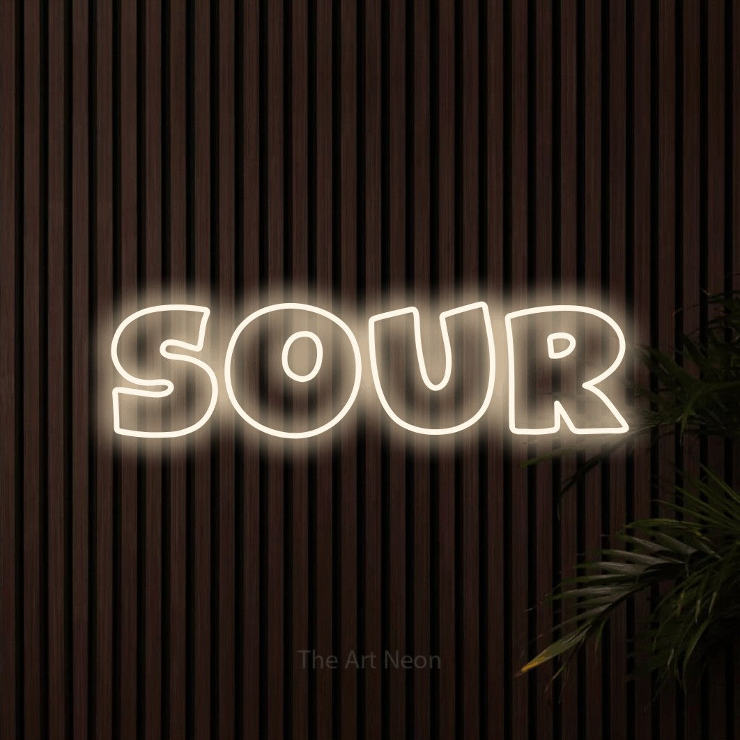 “Sour” LED neon sign in warm white, with wide lettering with irregular outlines, shown against dark wooden wall slats.