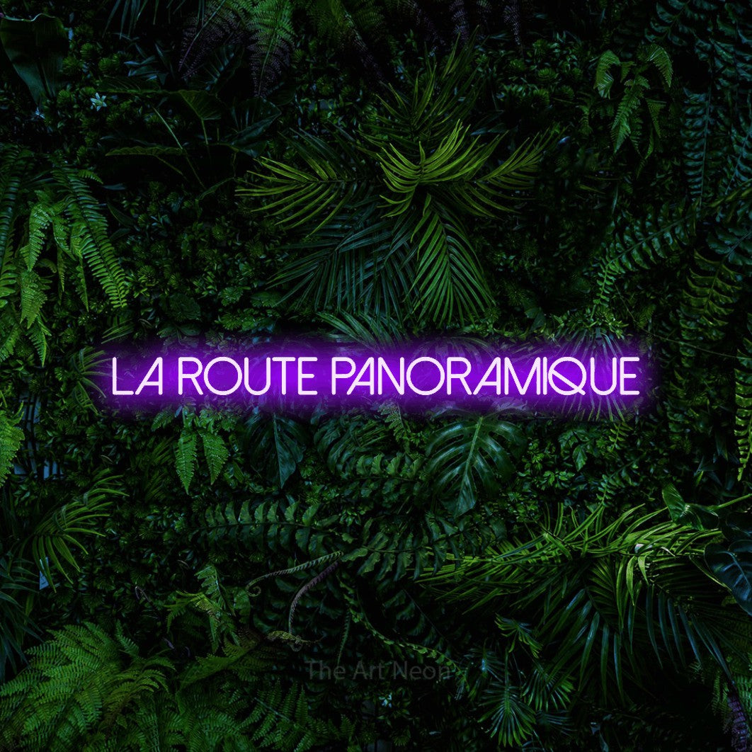“La route panoramique” LED neon sign in purple, with thin sans-serif lettering, shown against dense tropical foliage.