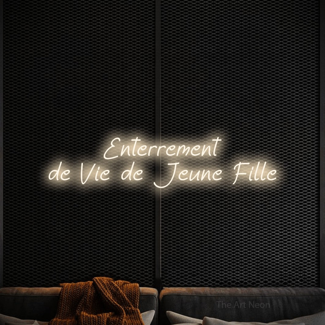 “Enterrement de vie de jeune fille” LED neon sign in warm white, with slanted handwritten lettering across 2 lines, shown against a modern dark-toned seating area.