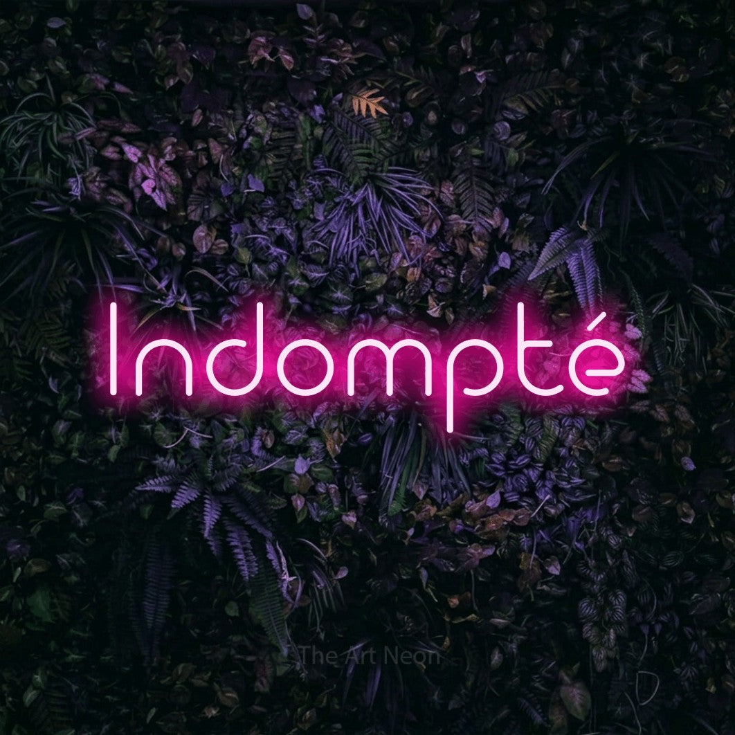 “Indompté” LED neon sign in hot pink, with stylised geometric lettering, shown against a dark wall with purple flowers.